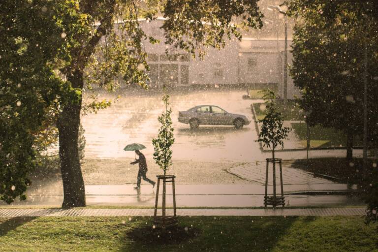 Wasser in der Stadt - Mann mit Regenschirm auf Parkplatz